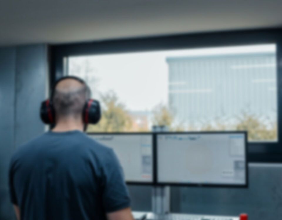 Mitarbeiter vor PC steuert CNC Maschine und fräst individuelle Carbon Teile